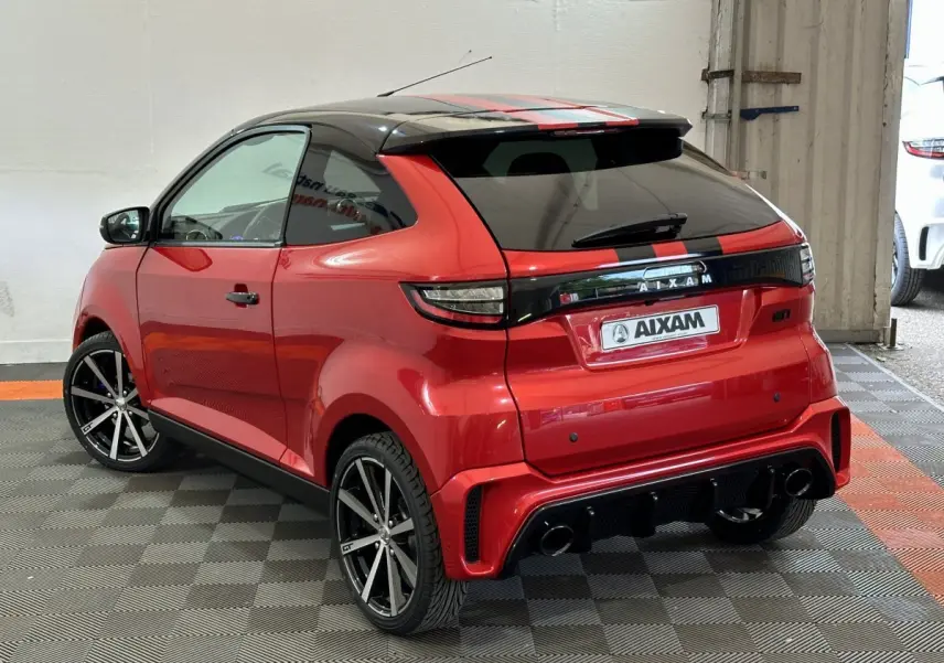 Vue 3/4 arrière droite de l'AIXAM Ambition rouge 2026 avec bandes noires, jantes sport et rétroviseur caméra côté gauche.