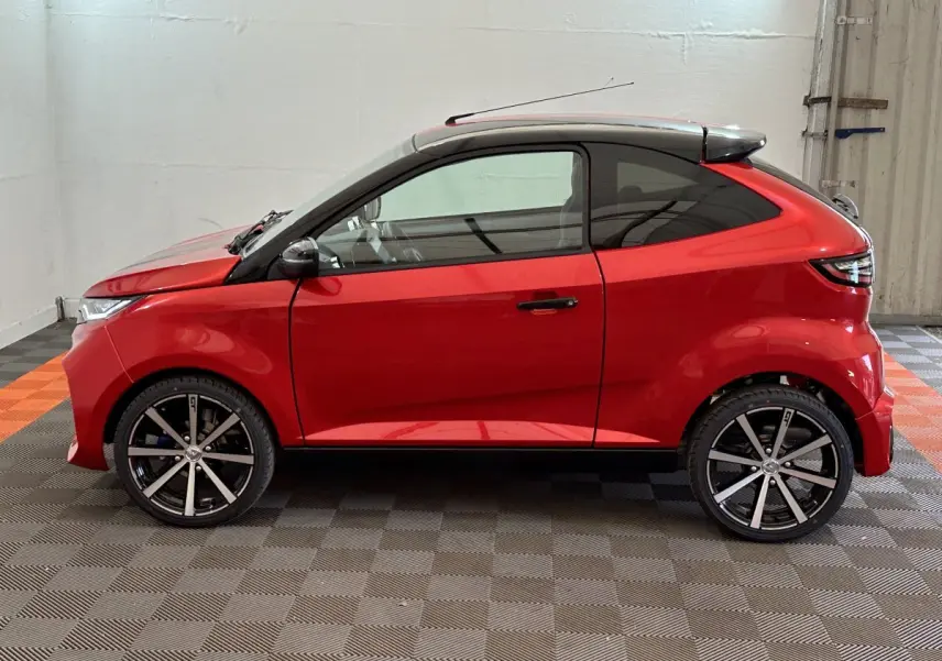 Vue de profil côté gauche d'une Aixam Ambition 0.5 City Coupe GTI rouge avec jantes noires et toit noir.