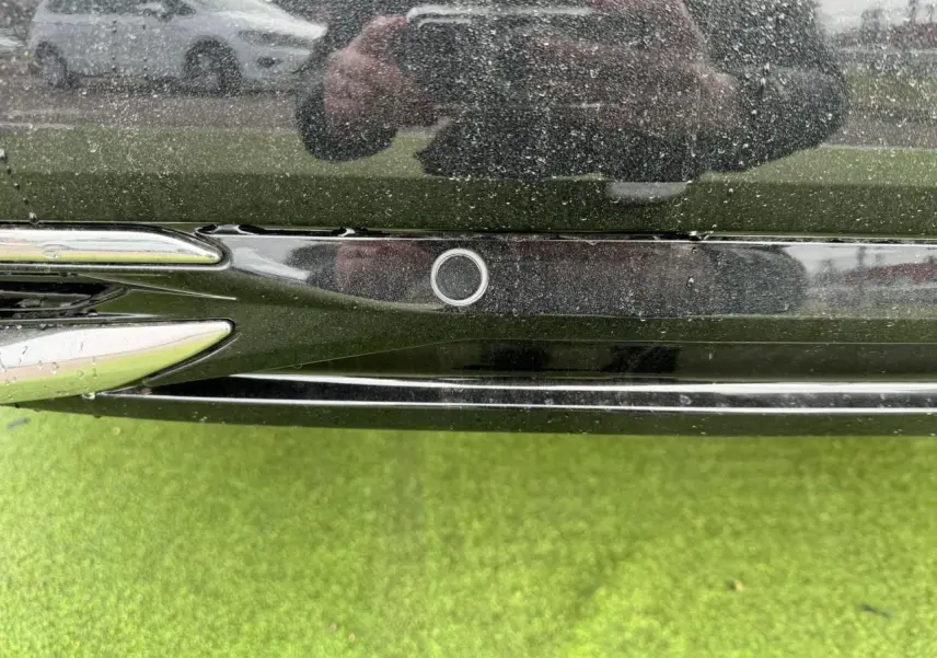 Gros plan sur le capteur de stationnement arrière noir du Peugeot 308 SW blanc Okenite, avec reflet et herbe verte en dessous.