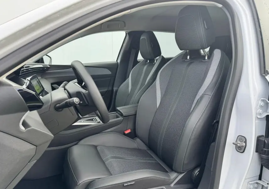 Vue intérieure côté conducteur de la Peugeot 308 SW 2024 blanc Okenite avec sièges tri matières noirs et gris à surpiqûres bleues.