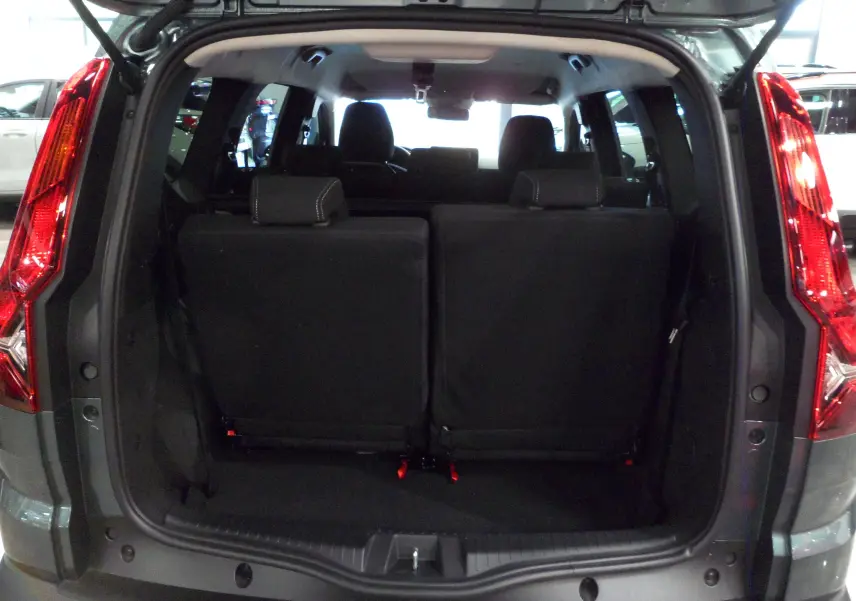 Vue arrière du coffre ouvert d'un Dacia Jogger 2025 vert cèdre, montrant les sièges arrière en tissu noir relevés.