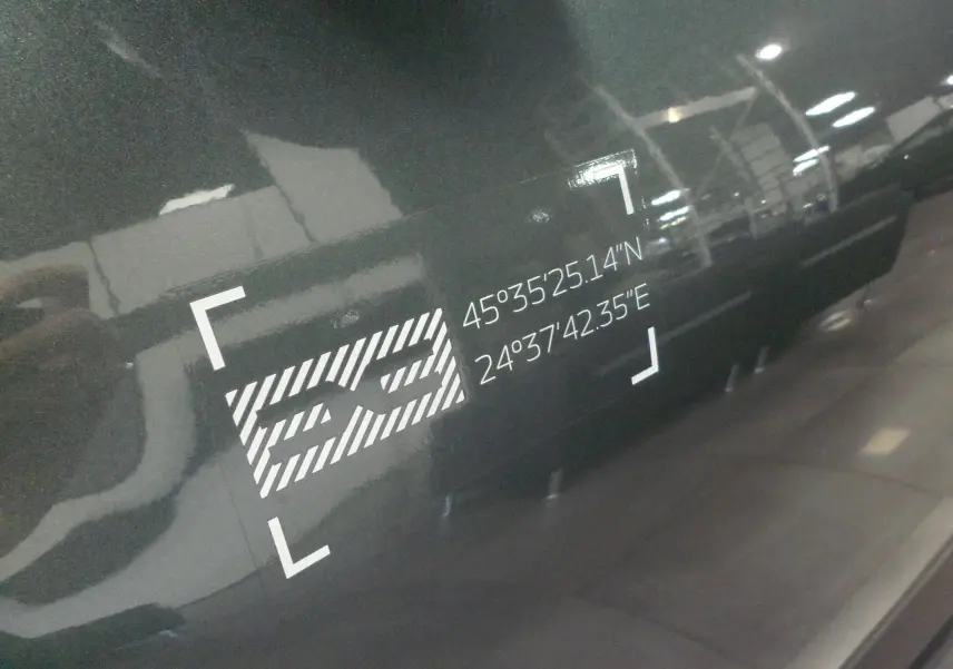 Gros plan sur l'autocollant "SS" avec coordonnées GPS sur la porte latérale droite d'un Dacia Jogger Vert Cèdre.