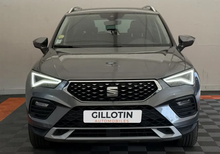 Vue frontale d'un SEAT Ateca gris clair 2023 avec phares LED allumés et calandre hexagonale noire.
