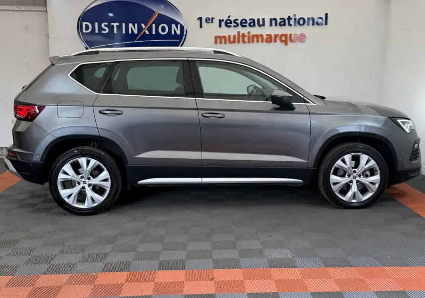 Profil droit d'un SEAT Ateca gris clair 2023, SUV compact avec jantes alliage et barres de toit chromées visibles.