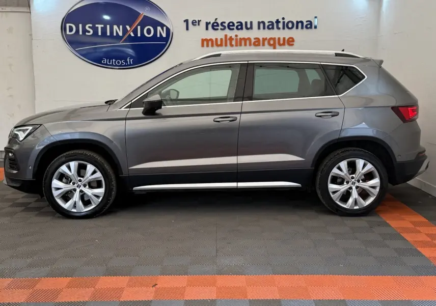 Profil côté gauche d'un SUV SEAT Ateca gris clair 2023 avec jantes alliage et barres de toit chromées.