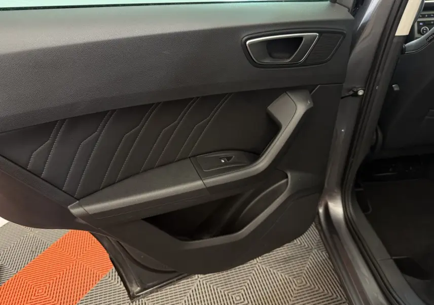 Vue intérieure du côté arrière gauche de la porte d’un SEAT Ateca gris clair, avec garniture en cuir noir et bouton de fenêtre électrique.