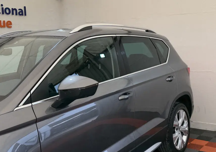 Vue latérale côté gauche d'un SEAT Ateca gris clair avec barres de toit chromées et jantes alliage.