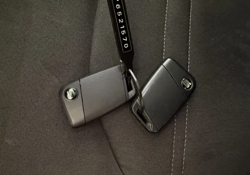 Gros plan sur deux clés noires SEAT posées sur une assise de siège en tissu gris foncé avec surpiqûres blanches.