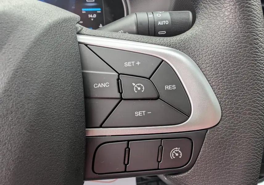 Gros plan sur les commandes du régulateur de vitesse au volant du Iveco Daily 35S16 blanc, tableau de bord en arrière-plan.