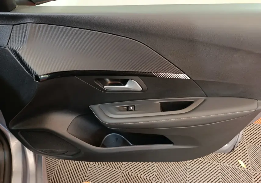 Vue intérieure côté gauche de la porte avant d'une Peugeot 208 gris clair avec insert effet carbone et commandes de vitre.