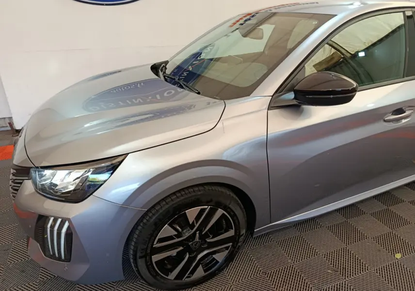 Vue 3/4 avant gauche d'une Peugeot 208 PureTech 100 S&S Allure gris clair avec jantes noires et rétroviseur noir.