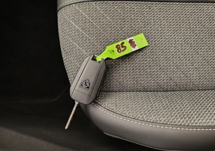 Clé Peugeot posée sur un siège avant en tissu gris à surpiqûres blanches, intérieur de Peugeot 208 2025.