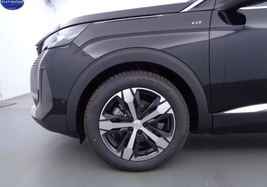 Gros plan sur la roue avant gauche et l'aile d'un Peugeot 3008 GT noir Perla Nera avec jante alu bicolore.