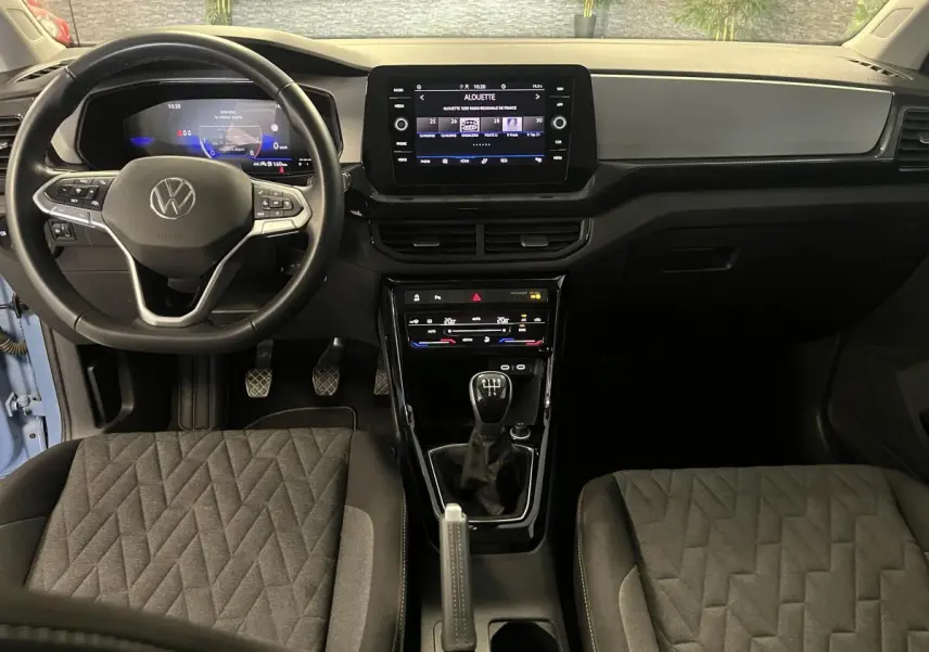 Intérieur du Volkswagen T-Cross 2024 bleu clair, vue frontale du tableau de bord avec volant cuir et levier manuel.