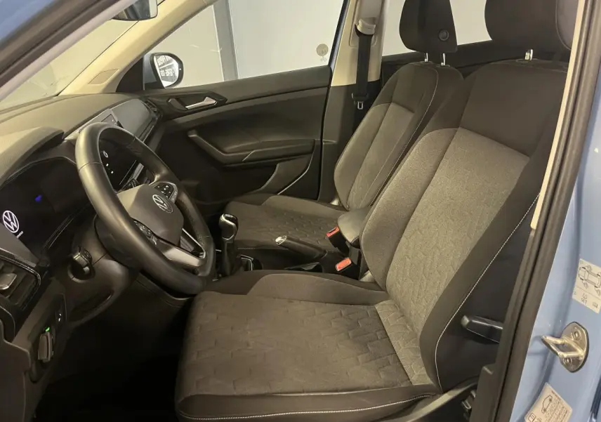 Intérieur avant du Volkswagen T-Cross bleu clair 2024, sièges tissu gris et volant multifonction en cuir visible côté conducteur.