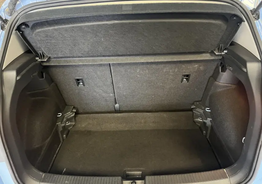 Coffre ouvert du Volkswagen T-Cross bleu clair 2024, montrant l'espace de rangement intérieur vide et les finitions en tissu noir.