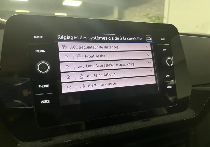 Écran tactile central du Volkswagen T-Cross 2024 affichant les réglages des aides à la conduite dans l'habitacle noir.