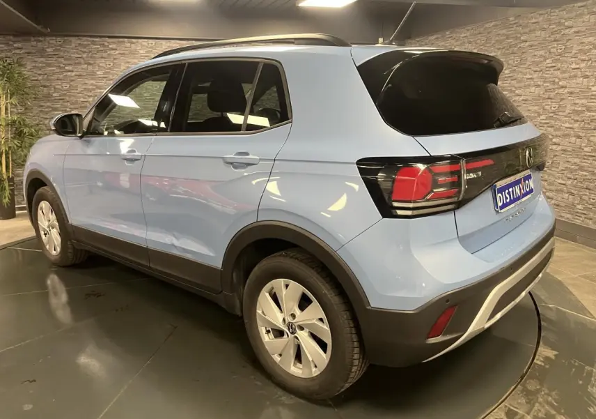 Vue 3/4 arrière droit d'un Volkswagen T-Cross bleu clair avec vitres arrière surteintées en intérieur showroom.