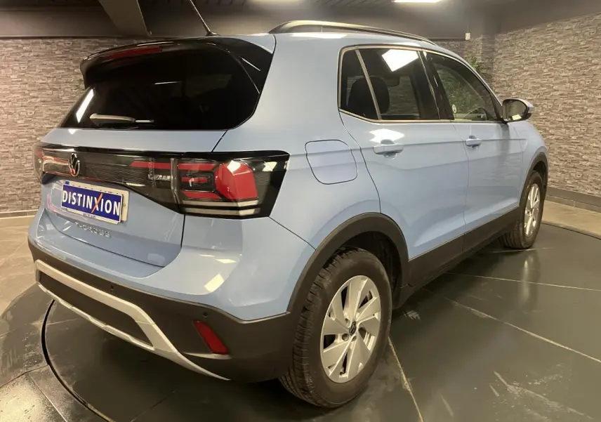 Volkswagen T-Cross bleu clair en 3/4 arrière droit, vitres arrière surteintées et jantes alliage argent.
