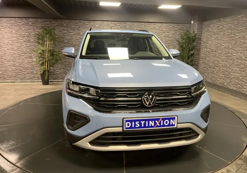 Volkswagen T-Cross bleu clair vue de face en intérieur, avec calandre noire et logo VW central bien visible.