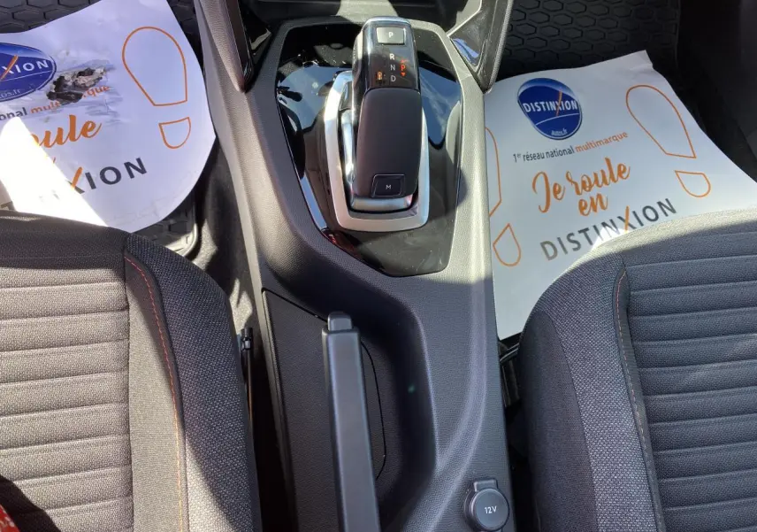 Vue plongeante sur la console centrale et levier de vitesse de la Peugeot 2008 bleu, avec sièges tissu gris et surpiqûres orange.
