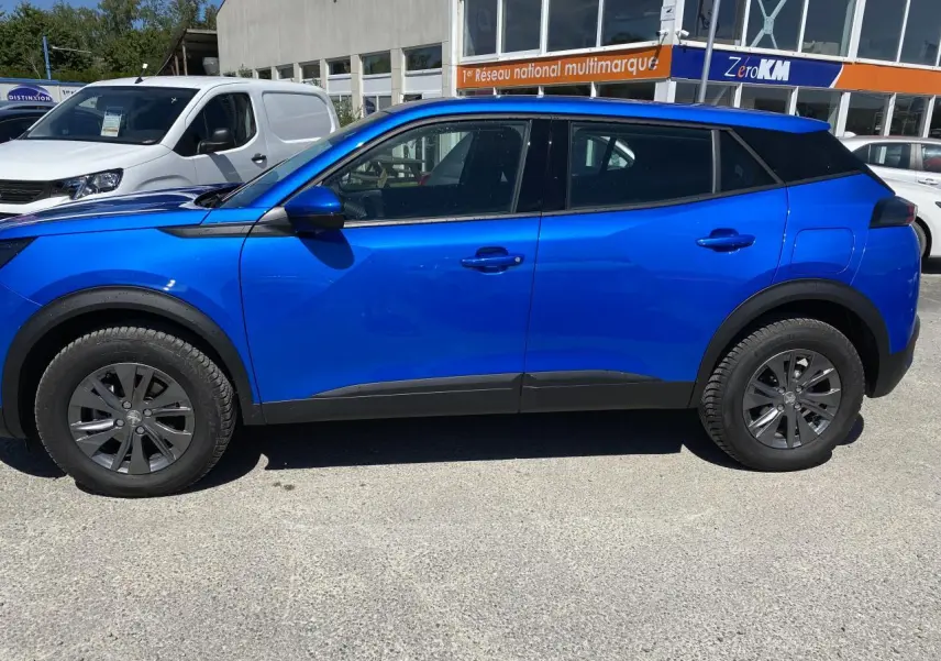 Profil côté gauche d'un Peugeot 2008 bleu 2021 Active Pack avec jantes foncées et protections noires sur les bas de caisse.