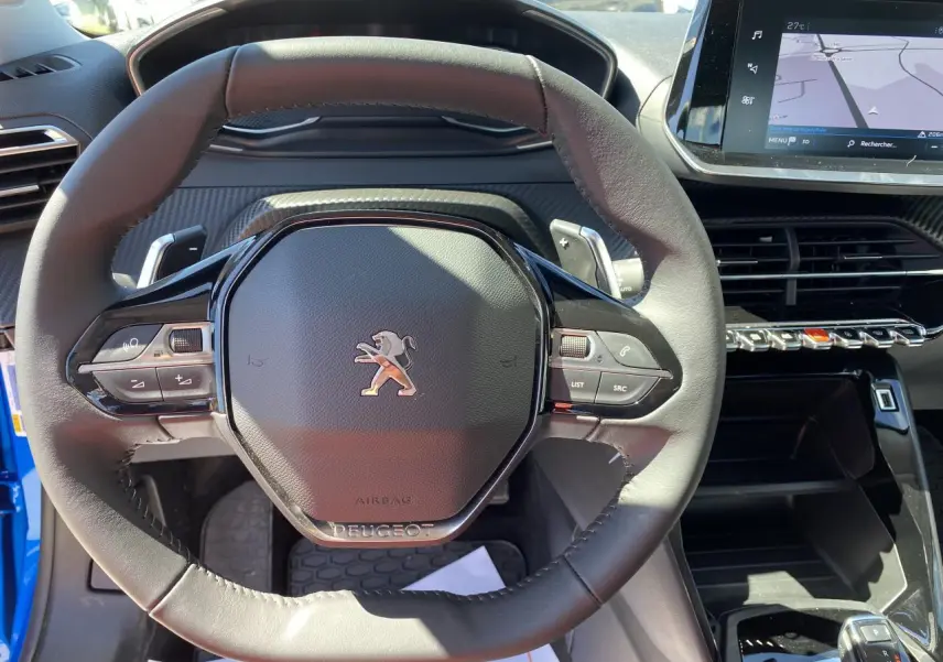 Vue rapprochée du volant cuir noir d'une Peugeot 2008 bleu 2021 avec tableau de bord et écran tactile visible.