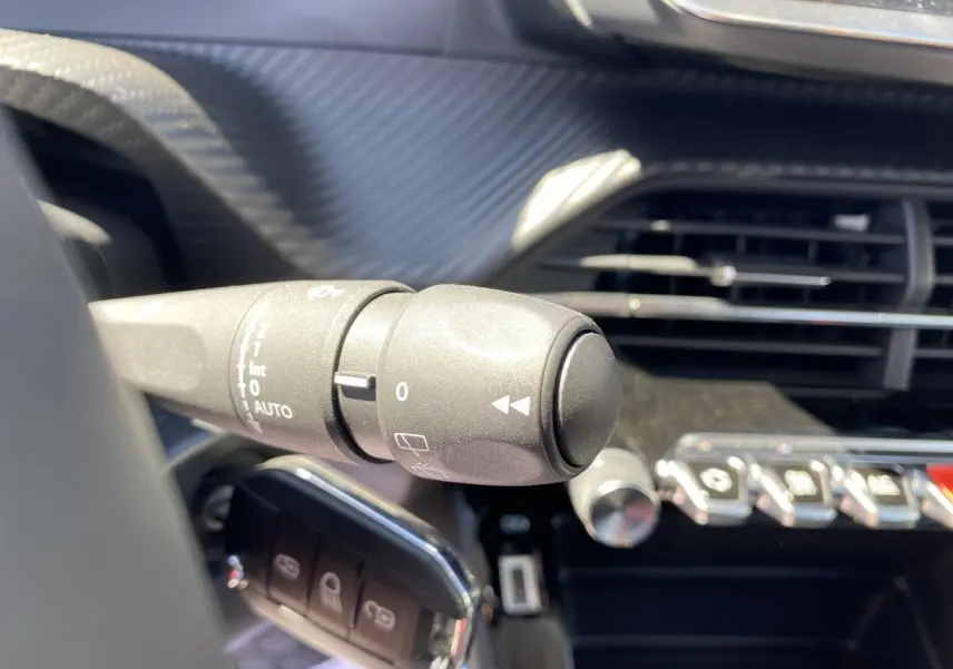 Gros plan sur la commande d'essuie-glace à gauche du volant dans l'habitacle noir d'un Peugeot 2008 bleu 2021.