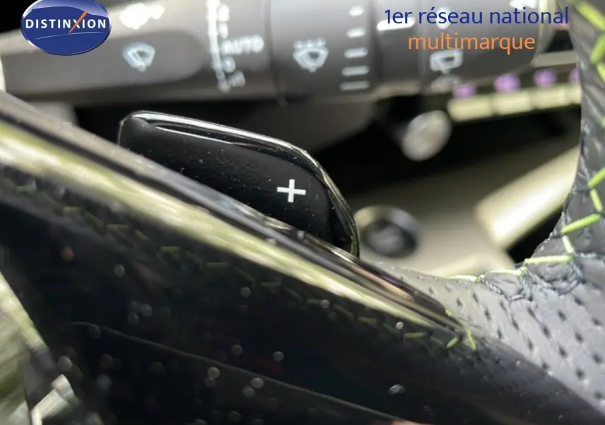 Gros plan sur la palette de changement de vitesse + au volant cuir noir avec surpiqûres vertes du Peugeot 308 gris Artense hybride.