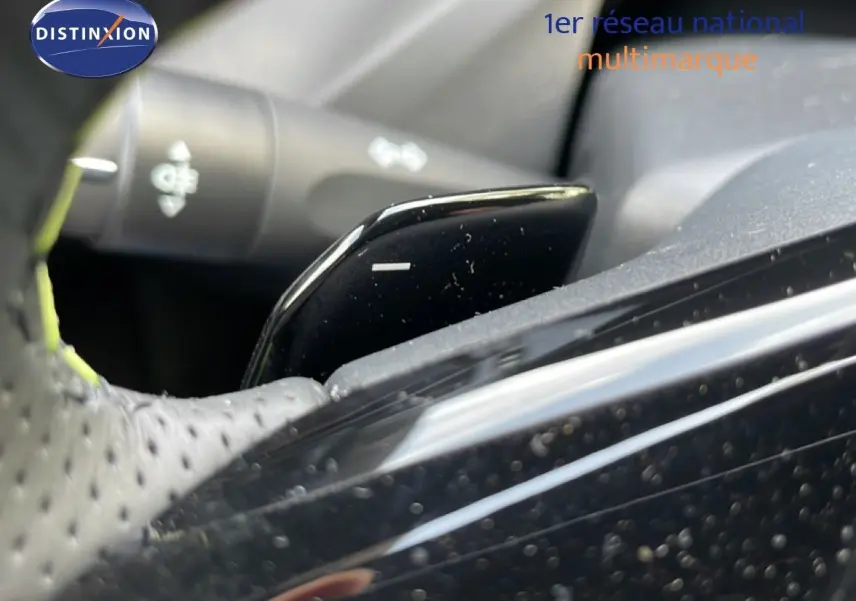 Gros plan sur la palette de changement de vitesse noire du volant perforé d’une Peugeot 308 gris Artense hybride.
