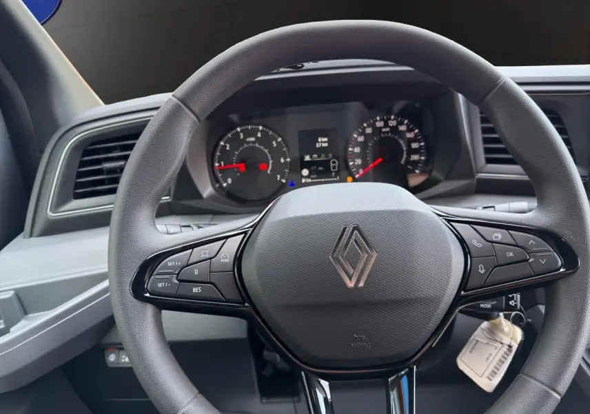 Vue rapprochée du volant gris du Renault Master 2026 avec commandes intégrées et tableau de bord numérique en arrière-plan.