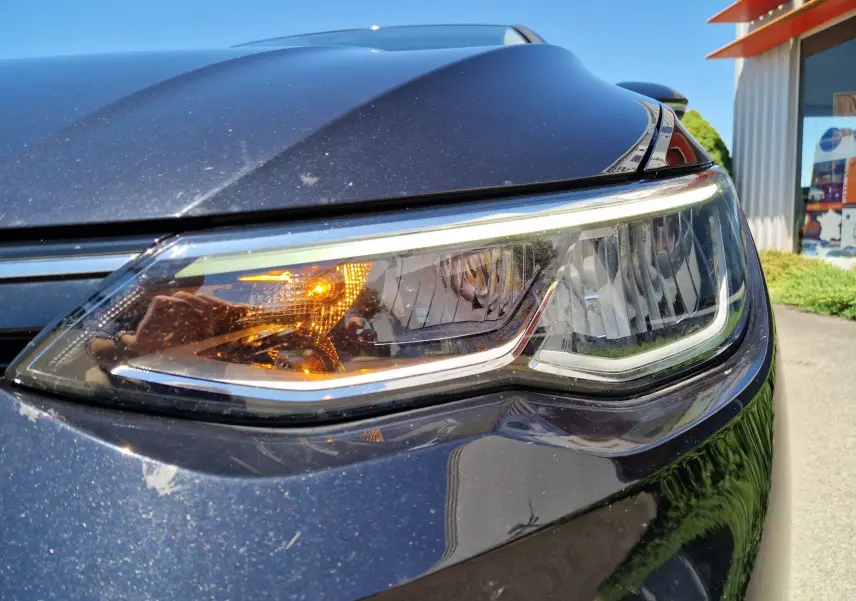 Gros plan sur le phare avant droit d'une Volkswagen Golf VIII noire métal, avec clignotant allumé.