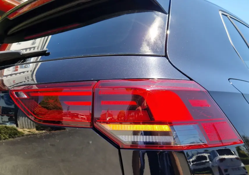Gros plan sur le feu arrière droit rouge et orange d'une Volkswagen Golf VIII noire métallisée sous lumière naturelle.