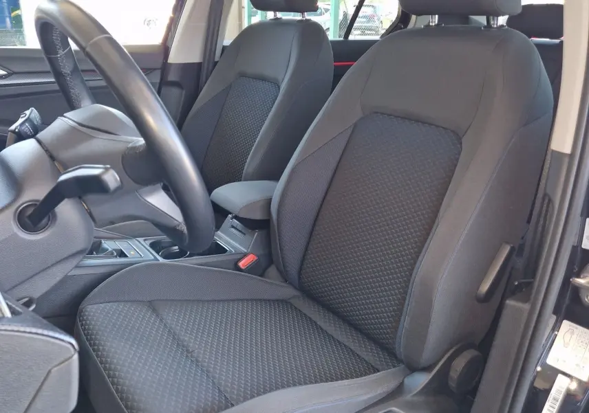 Vue intérieure côté conducteur de la Volkswagen Golf VIII noire, sièges tissu gris avec console centrale visible.