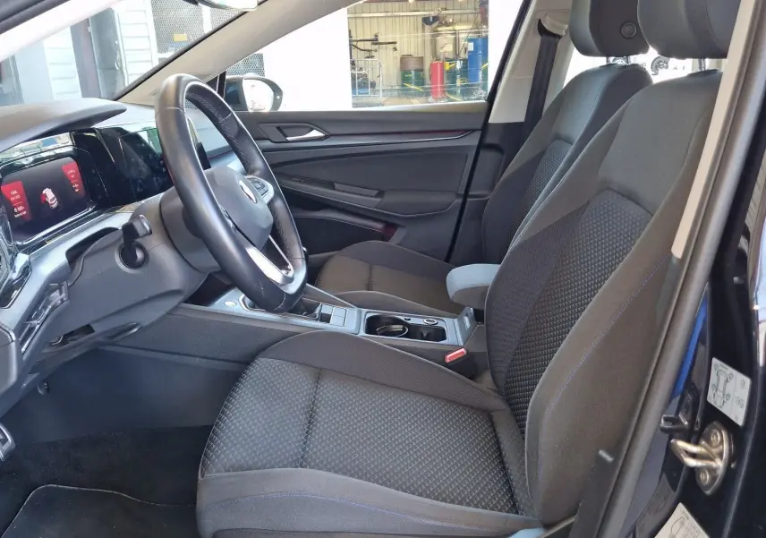 Intérieur de la Volkswagen Golf VIII 2.0 TDI noir métal, vue côté conducteur avec sièges tissu gris et tableau de bord moderne.