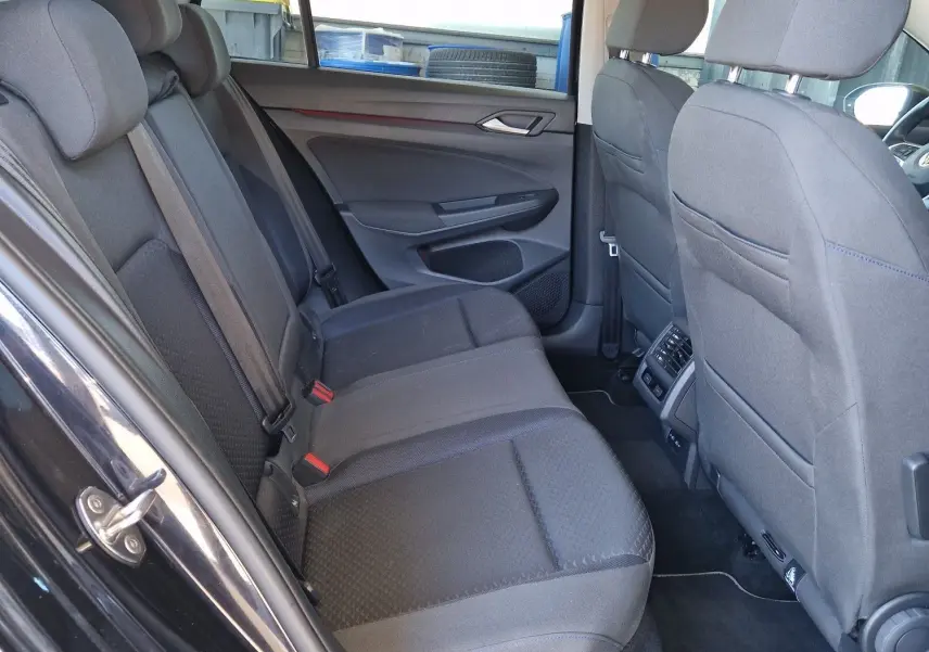 Vue intérieure côté gauche des sièges arrière gris tissu de la Volkswagen Golf VIII noire métal, avec portières ouvertes.