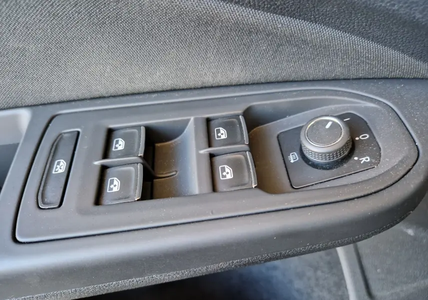 Gros plan sur les commandes de lève-vitres et réglage des rétroviseurs côté conducteur d'une Volkswagen Golf VIII noire.