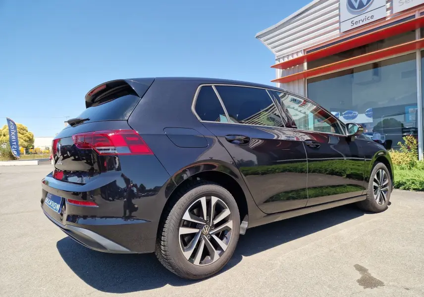 Volkswagen Golf VIII 2.0 TDI noire métal vue 3/4 arrière droit, stationnée devant un service Volkswagen.
