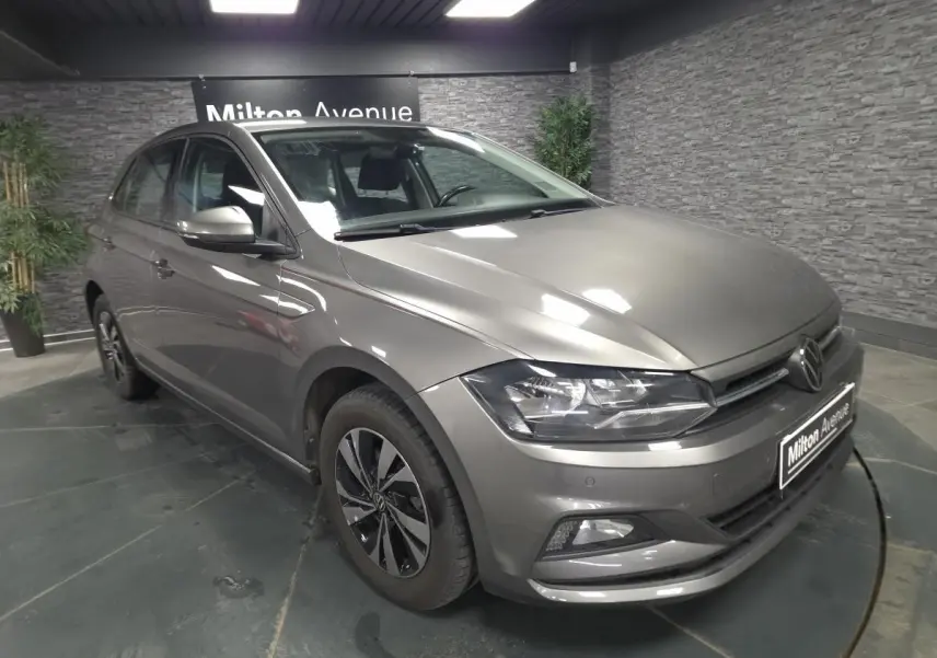 Volkswagen Polo gris 3/4 avant droit avec jantes alliage et phares LED dans showroom.