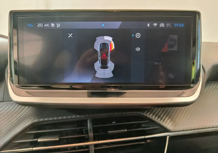 Écran tactile central de la Peugeot 208 PureTech 100 S&S Allure 2025 affichant l'aide au stationnement, intérieur gris foncé.