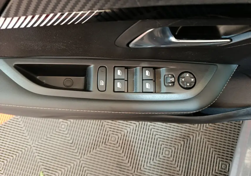 Panneau de commande des vitres et rétroviseurs côté conducteur de la Peugeot 208 gris foncé, vue intérieure rapprochée.