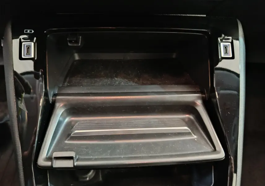 Gros plan sur la console centrale noire de la Peugeot 208 PureTech 100 S&S Allure avec compartiment ouvert et ports USB visibles.