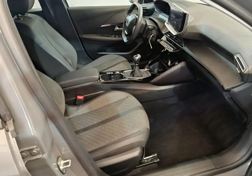 Vue intérieure côté conducteur de la Peugeot 208 PureTech 100 S&S Allure 2025 avec sièges gris et écran tactile central.
