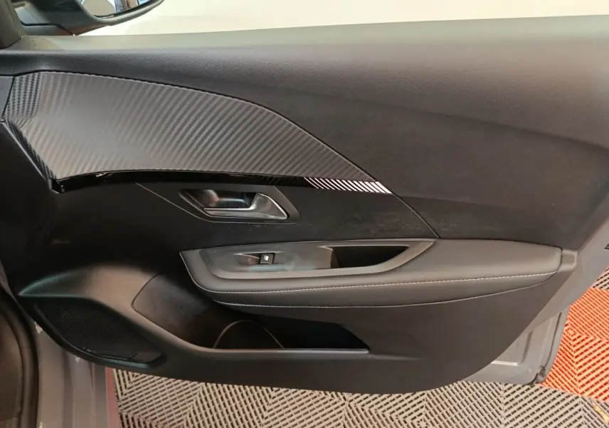 Vue rapprochée de la porte côté gauche de la Peugeot 208 gris foncé, avec insert décoratif effet carbone et commande de vitre.
