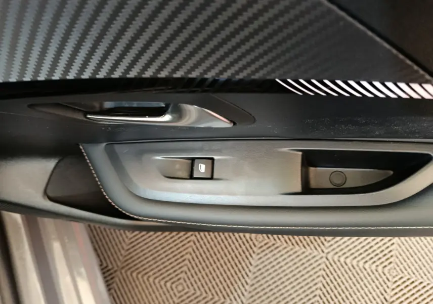 Gros plan sur la poignée intérieure côté gauche de la porte d'une Peugeot 208 gris foncé avec bouton de lève-vitre.