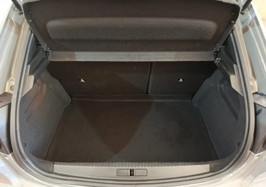 Coffre ouvert d'une Peugeot 208 gris foncé, vue de dessus montrant l'espace de rangement vide et les garnitures intérieures noires.