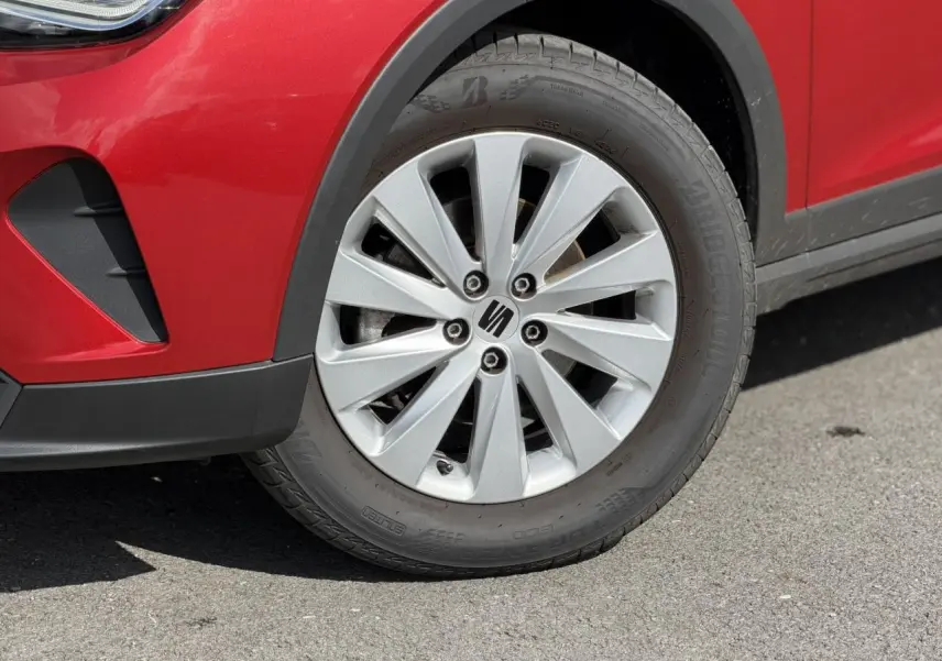 Gros plan sur la roue avant droite d'une SEAT Arona Rouge Désir avec jante alliage 16 pouces et partie du pare-chocs avant.