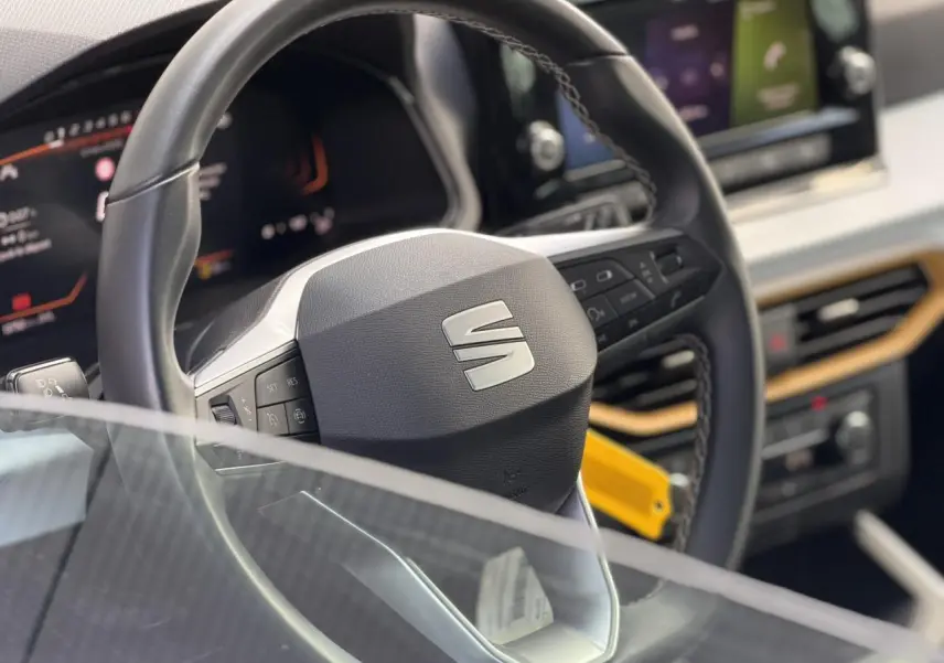 Gros plan sur le volant et le tableau de bord digital du SEAT Arona 2025, avec détails en noir et inserts bois clair.