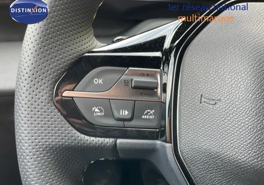Gros plan sur le volant en cuir perforé noir de la Peugeot 308 gris Artense, avec commandes intégrées visibles.