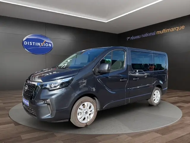 Vue 3/4 avant droit d'un Nissan Primastar gris foncé avec portes latérales, présenté en showroom.